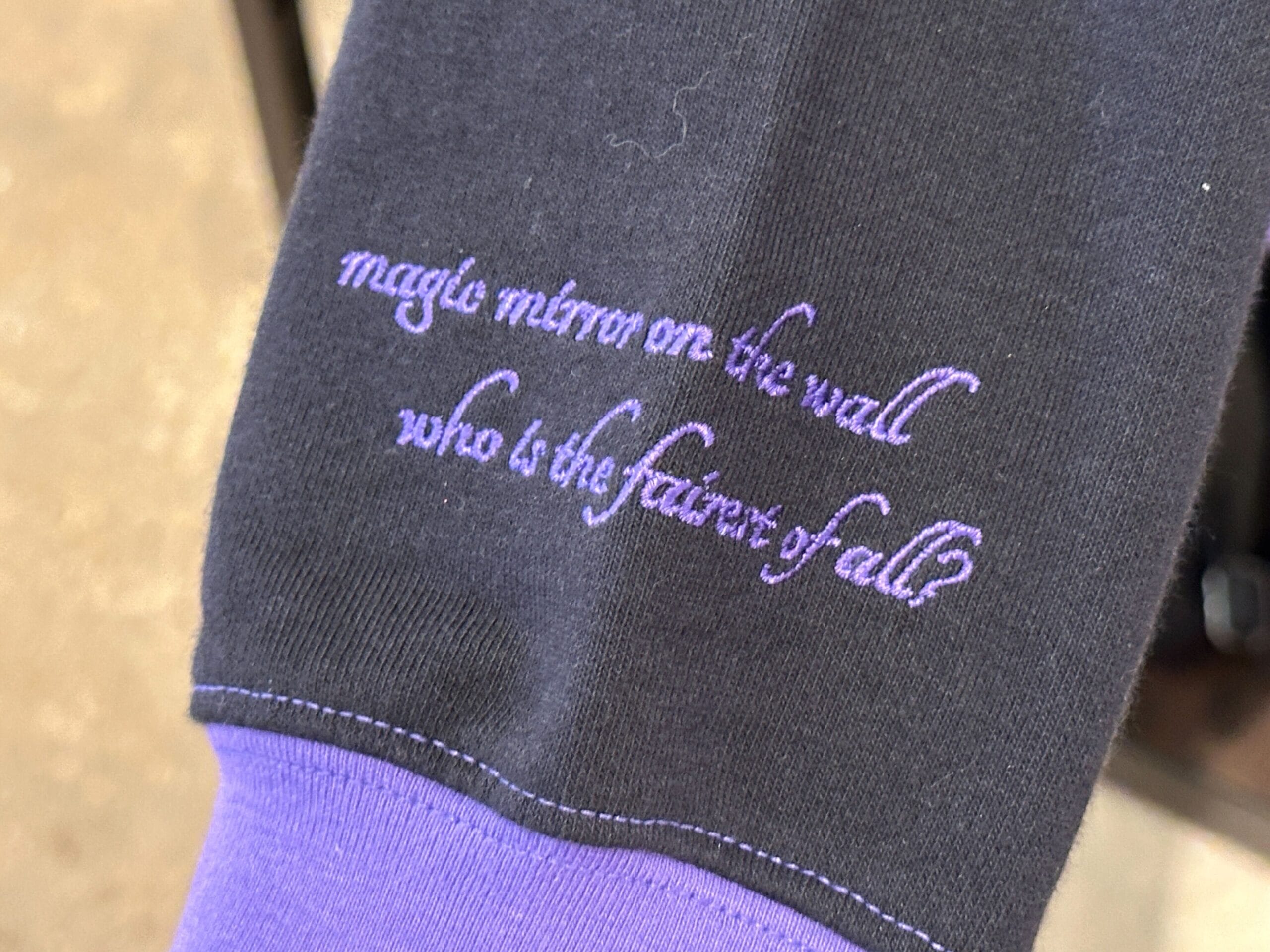 Tissu noir et violet brodé en cursive : 'magic mirror on the wall who is the fairest of all?'