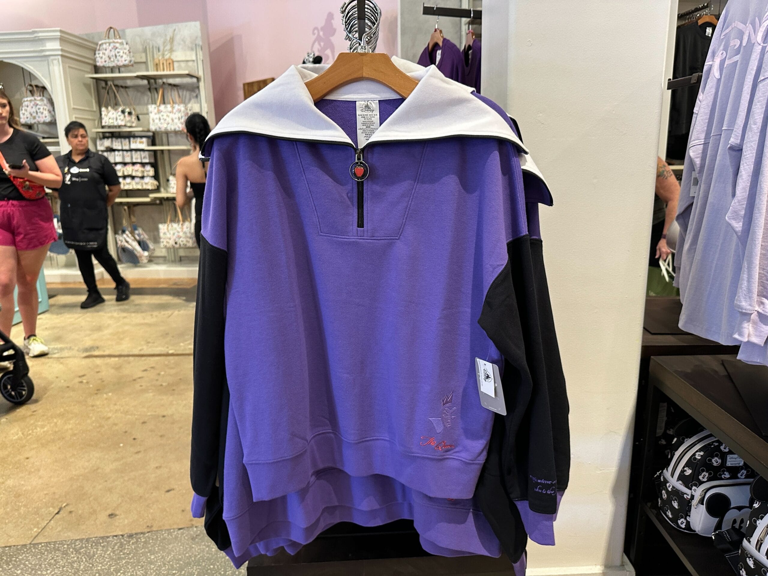 Sweatshirt violet et noir avec col blanc, présenté sur un cintre en magasin
