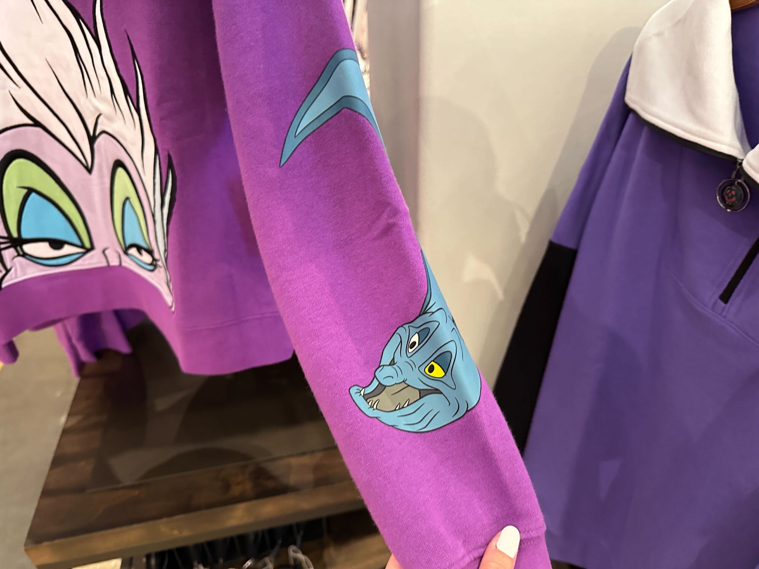 Zoom sur manche de sweat violet avec une anguille bleue et un visage de dessin animé en arrière-plan