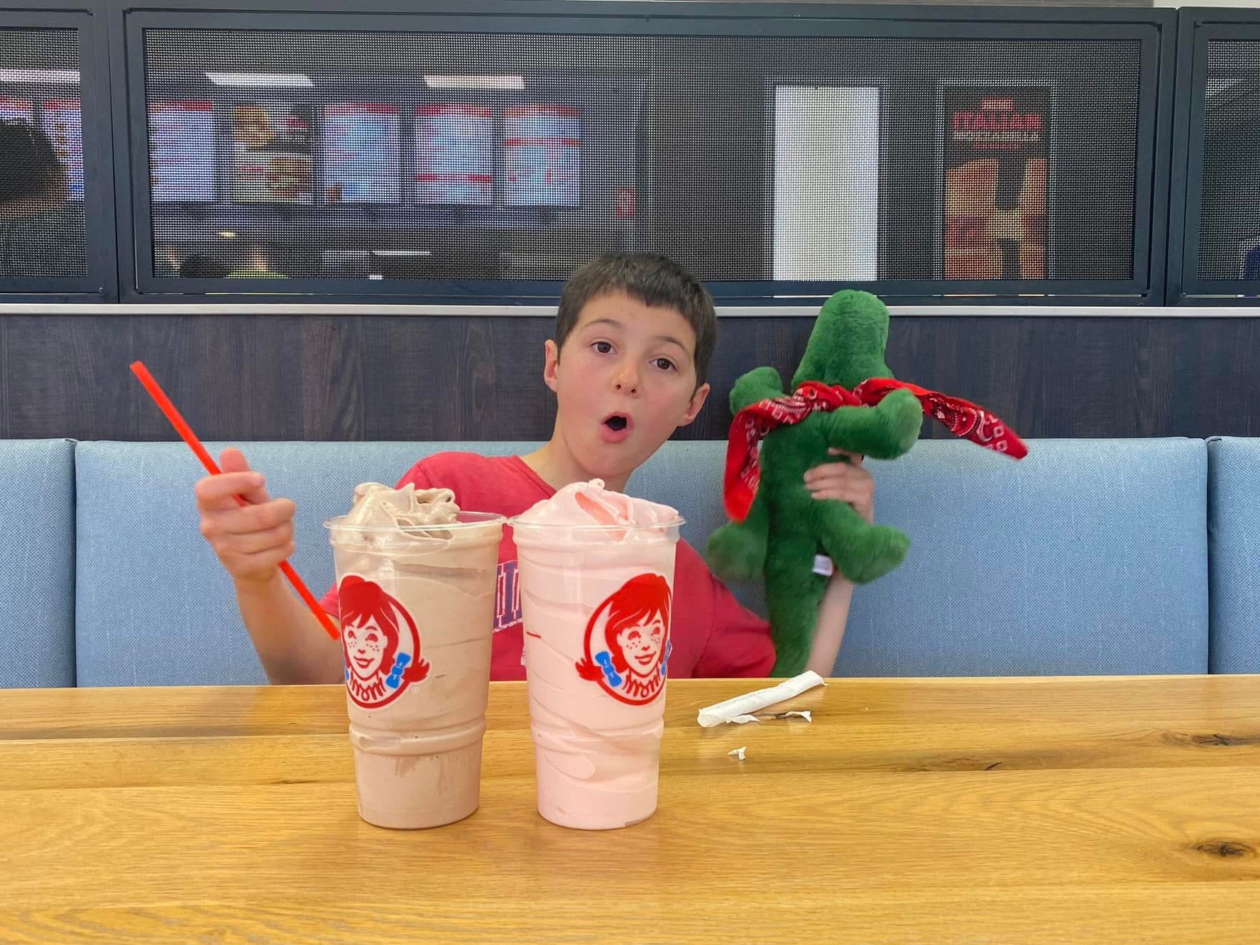 Un garçon pose avec un crocodile en peluche devant deux boissons glacées de Wendy's.
